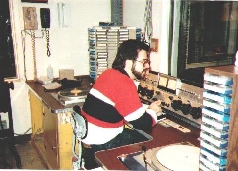 A young Jason cueing records at a radio station control board with turntables and a cart wall